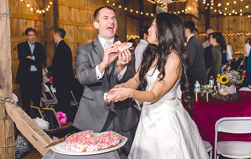 Bride and groom laughing while holding pieces of a giant doughnut