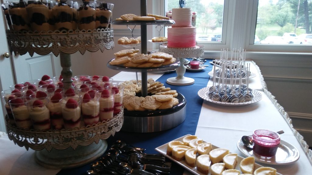 A dessert table loaded with shortbread cookies, cake pops, mini cheesecakes, and a pink and white wedding cake